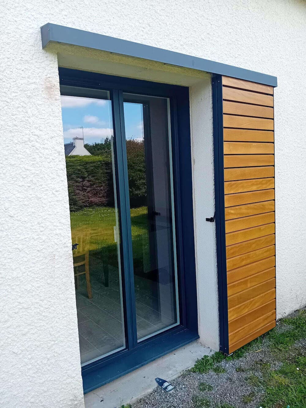 Porte-fenêtre coulissante bleu nuit avec habillage bois posée sur une façade blanche