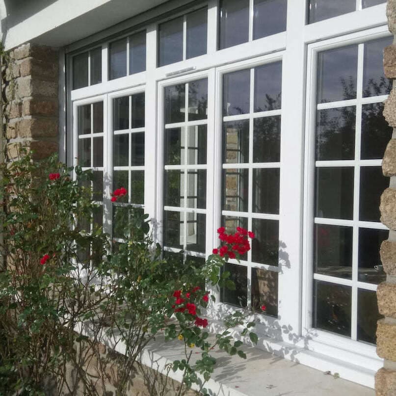 Fenêtres bois blanches à petits bois sur une façade en pierre garnie de rosiers
