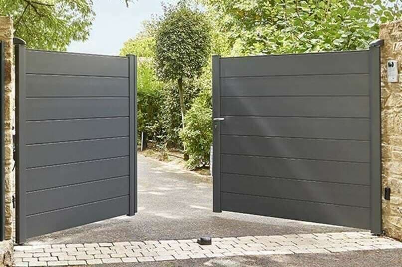 Portail battant en aluminium gris à lames horizontales, ouvert sur une allée bordée d'arbres