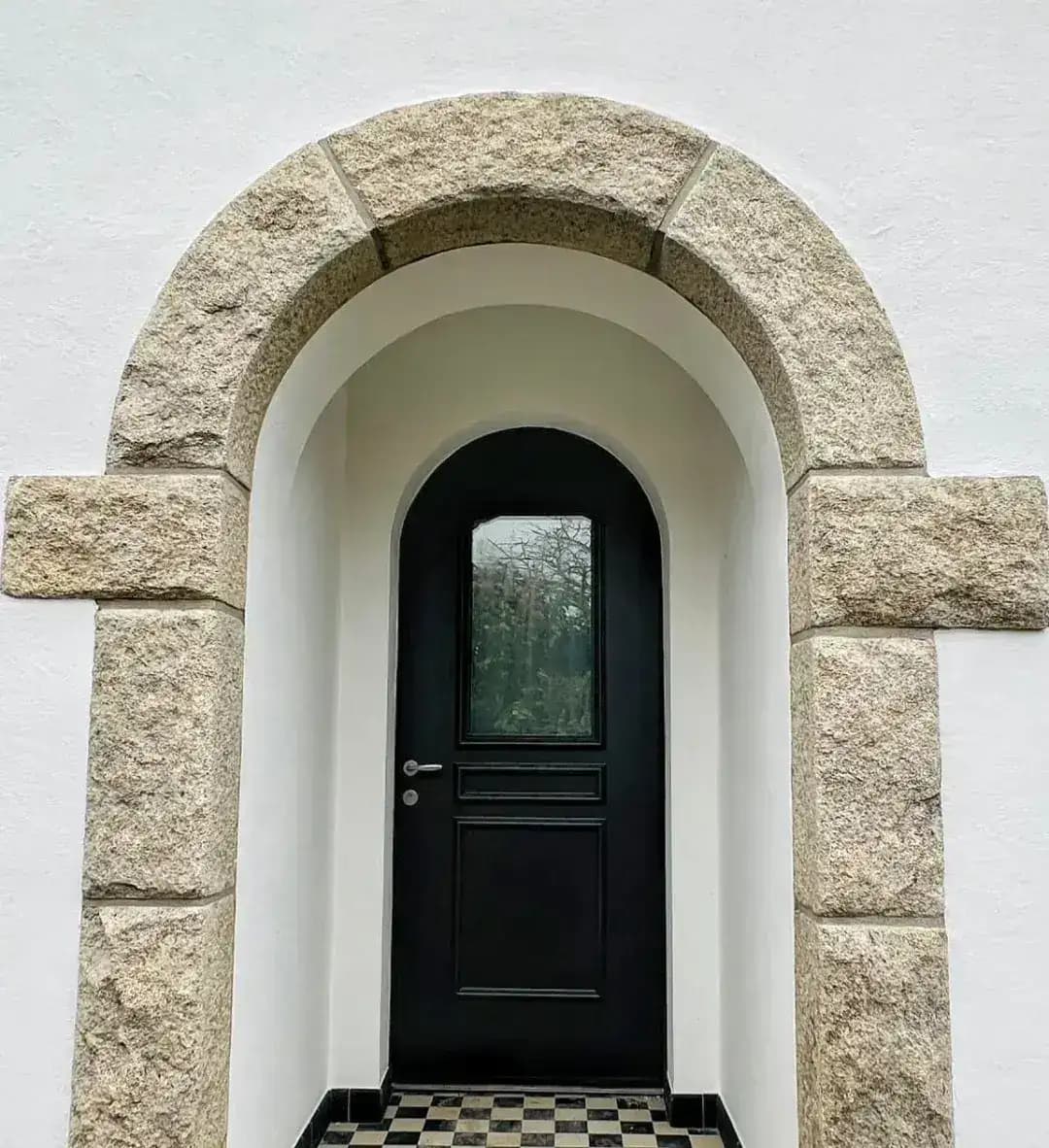 Porte d'entrée cintrée noire sous arche en granit