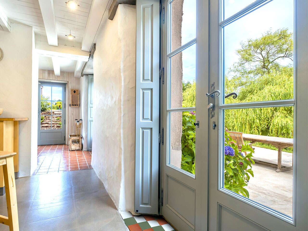 Porte-fenêtre bois bleu-gris ouverte sur la terrasse d'une maison en pierre
