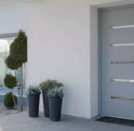 Porte d'entrée grise à poignées barres inox sur la façade blanche d'une maison contemporaine
