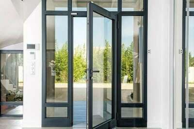 Porte d'entrée vitrée à profilés aluminium noirs, ouverte sur le jardin depuis une entrée blanche