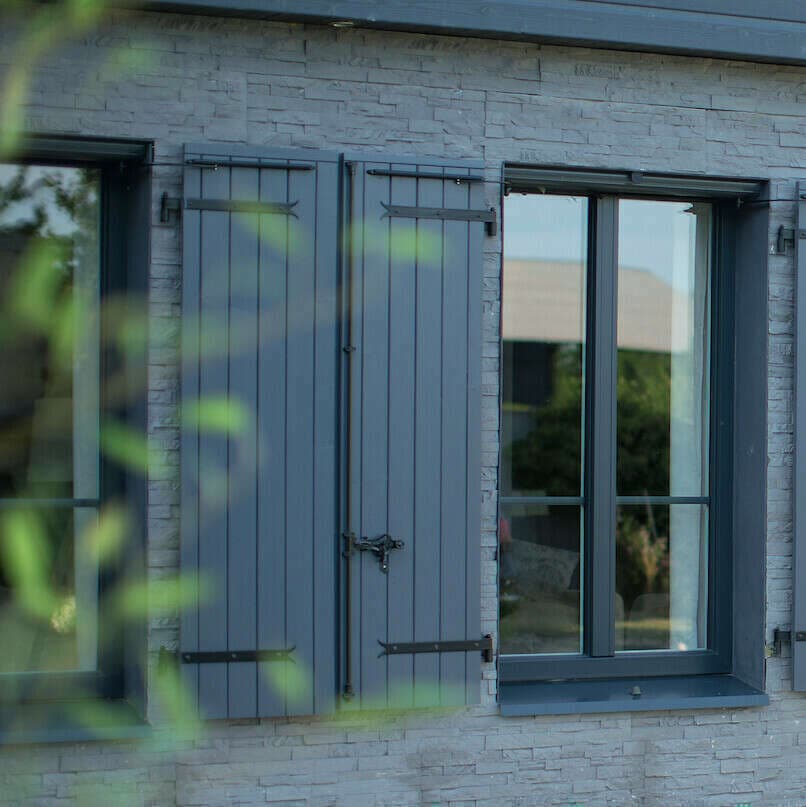 Volets battants en bois gris sur la façade en pierre claire d'une maison