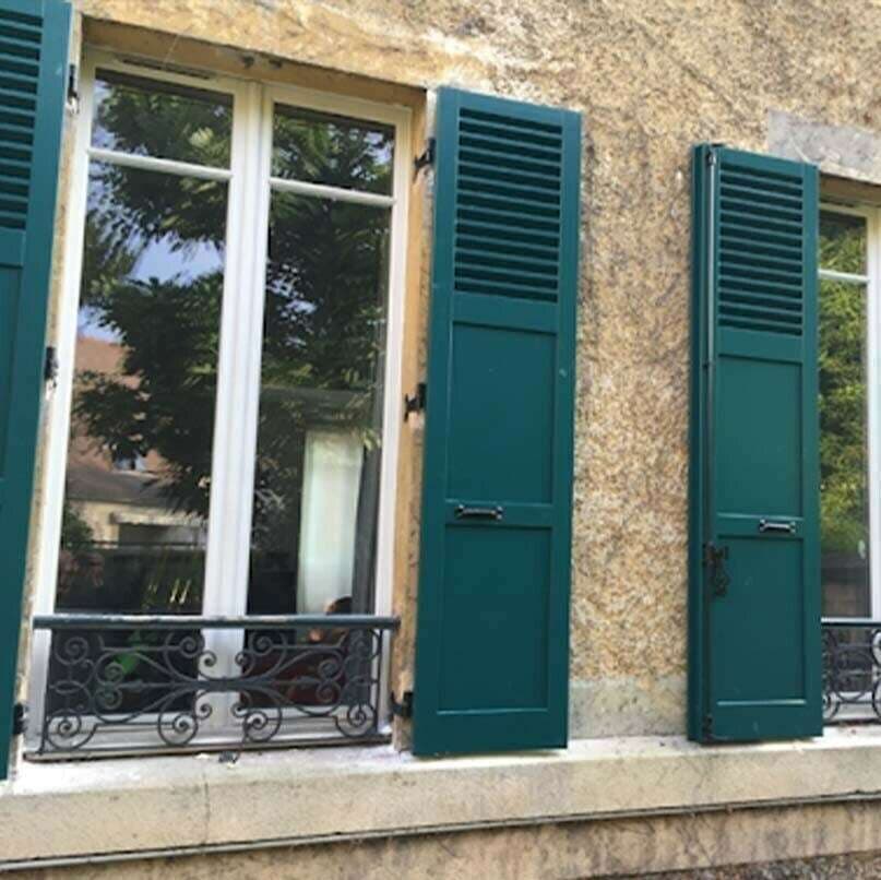 Volets battants persiennés vert bouteille sur la façade en pierre d'une maison ancienne