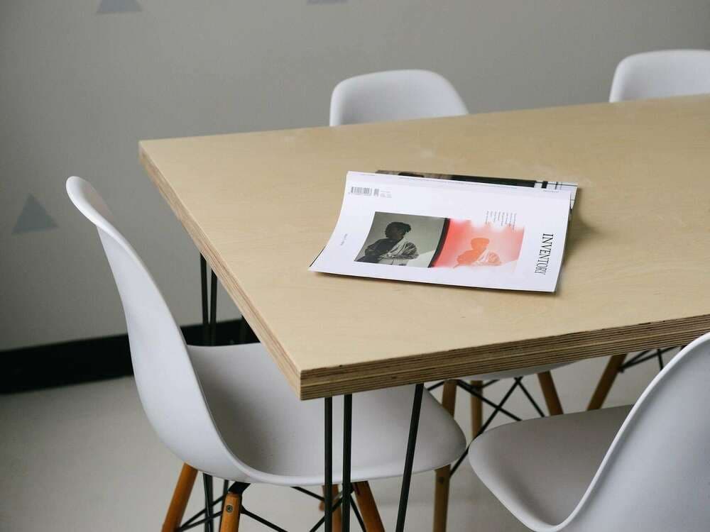 Magazine ouvert sur une table en bois clair entourée de chaises blanches